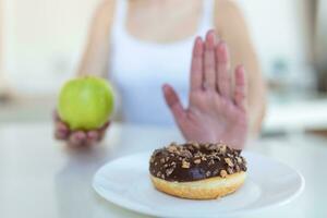 dieet of mooi zo Gezondheid concept. jong vrouw afwijzen rommel voedsel of ongezond voedsel zo net zo donut of toetje en kiezen gezond voedsel zo net zo vers fruit of groente. foto