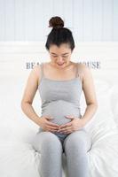zwangere vrouw zittend op het bed en haar buik thuis aan te raken.