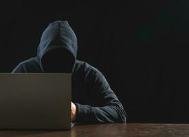hacker spion Mens een persoon in zwart capuchon zittend Aan een tafel op zoek computer laptop gebruikt Log in wachtwoord aanval veiligheid naar circuleren gegevens digitaal in internet netwerk systeem, nacht donker achtergrond. foto