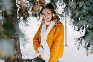 tiener blond in een geel trui buiten in winter. een tiener- meisje Aan een wandelen in winter kleren in een besneeuwd Woud foto