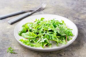 een mengsel van vers rucola, snijbiet en mizun bladeren Aan een bord en vorken Aan de tafel. vegetarisme, gezond aan het eten foto