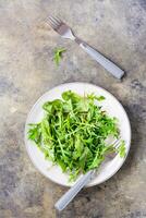 een mengsel van vers rucola, snijbiet en mizun bladeren Aan een bord en vorken Aan de tafel. vegetarisme, gezond aan het eten. top en verticaal visie foto