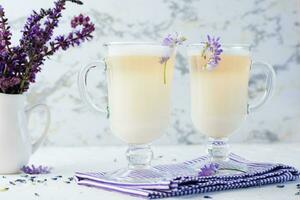 latte met melk, schuim en lavendel in bril en een boeket van bloemen in een kruik Aan een wit tafel. aromatisch koffie foto