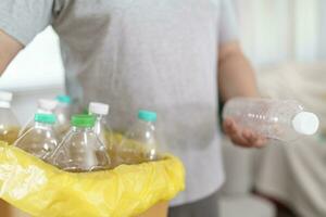 huis recycle eco groen nul concept Mens het werpen leeg plastic fles in recycling bak met geel vuilnis Tassen Bij huis foto