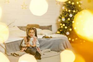 weinig meisje leugens Aan een bed in een kamer versierd voor Kerstmis foto