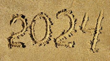 de getallen 2024 zijn geschreven Aan de zanderig strand. de concept van de nieuw jaar foto