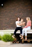 familie met een moeder, vader en dochter zittend buiten Aan de stappen van een voorkant veranda van een steen huis foto