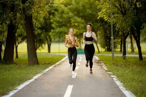 twee mooi jong Dames rennen Aan de rijbaan in de park foto