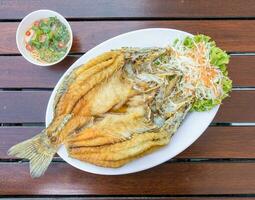 gebakken snapper vis blanco in wit bord Aan hout tafel geserveerd met vis saus en groenten. foto