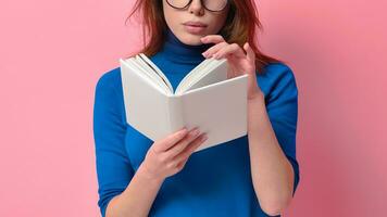 bijgesneden portret van zelfverzekerd jong volwassen vrouw met een aantrekkelijk kapsel en bril Holding een boek met een leeg omslag. geïsoleerd Aan een roze gekleurde achtergrond. gefocust Aan lezing. foto