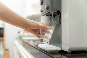 detailopname hand- van vrouw drinken water is gegoten van water koeler in de glas, drinken water machine foto