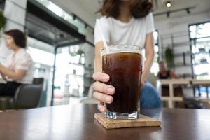close-up vrouw hand met ijs zwarte koffie in coffeeshop foto