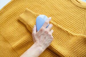 vrouw in geel trui gebruik makend van kleding stof pillen Verwijderen gereedschap foto
