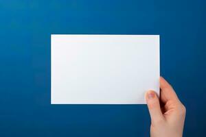 een menselijk hand- Holding een blanco vel van wit papier of kaart geïsoleerd Aan blauw achtergrond. ai gegenereerd foto