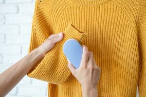 vrouw in geel trui gebruik makend van kleding stof pillen Verwijderen gereedschap foto