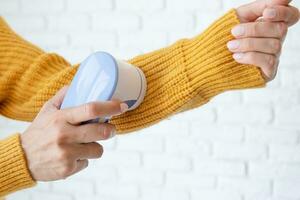 vrouw in geel trui gebruik makend van kleding stof pillen Verwijderen gereedschap foto