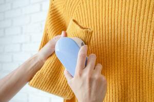 vrouw in geel trui gebruik makend van kleding stof pillen Verwijderen gereedschap foto