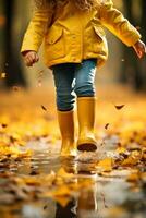 kind in geel rubber laarzen genieten van jumping over- plassen in de regen gedurende herfst seizoen foto