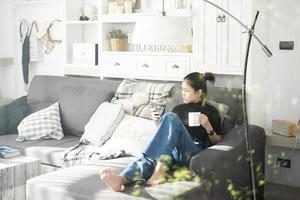 jonge mooie vrouw ontspannen op de bank thuis en het gebruik van slimme telefoon foto