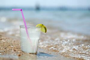 glas van limonade of water Aan strand door zee foto