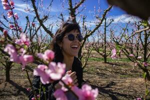 vrouw glimlacht tussen de mooi roze bloemen van de perzik boom. foto