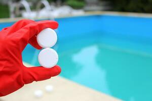 wit klein chloor- tablet in de hand- van een rood beschermend handschoen van een zwembad ontsmetting onderhoud arbeider. de begin van de zwemmen seizoen in de heet zomer Aan vakantie. foto