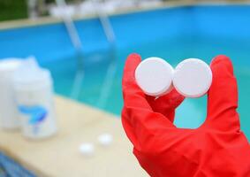 wit klein chloor- tablet in de hand- van een rood beschermend handschoen van een zwembad ontsmetting onderhoud arbeider. de begin van de zwemmen seizoen in de heet zomer Aan vakantie. foto