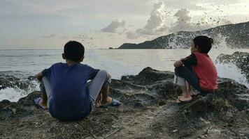 twee broers zittend Aan de rots aan het kijken de zee Bij zonsondergang, Kuta mandala, lombok, Indonesië foto