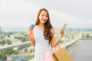portret mooie jonge aziatische vrouw blij en glimlach met creditcard en mobiel of smartphone en boodschappentas foto