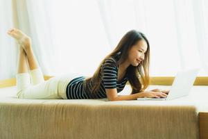 portret mooie jonge aziatische vrouw die computernotitieboekje of laptop op bank in woonkamer gebruikt foto