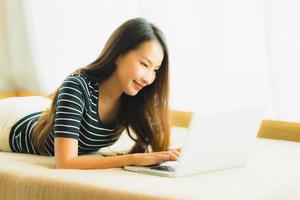 portret mooie jonge aziatische vrouw die computernotitieboekje of laptop op bank in woonkamer gebruikt foto