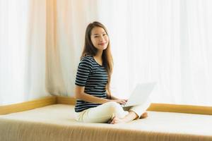 portret mooie jonge aziatische vrouw die computernotitieboekje of laptop op bank in woonkamer gebruikt foto