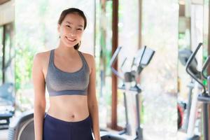 portret mooie jonge aziatische vrouw oefenen met fitnessapparatuur in sportschool interieur foto