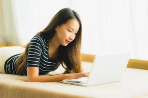 portret mooie jonge aziatische vrouw die computernotitieboekje of laptop op bank in woonkamer gebruikt foto