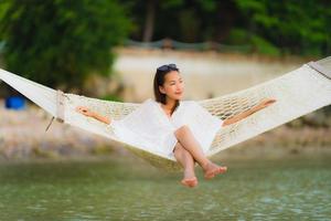 portret mooie jonge aziatische vrouw zittend op een hangmat rond zee strand oceaan om te ontspannen foto