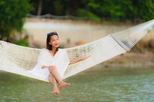 portret mooie jonge aziatische vrouw zittend op een hangmat rond zee strand oceaan om te ontspannen foto