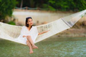 portret mooie jonge aziatische vrouw zittend op een hangmat rond zee strand oceaan om te ontspannen foto