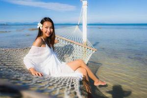 portret mooie jonge aziatische vrouw zittend op een hangmat rond zee strand oceaan om te ontspannen foto