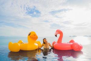 portret jonge aziatische vrouw op opblaasbare vlotter gele eend en roze flamingo rond het buitenzwembad in hotel en resort foto