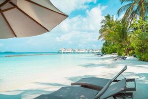 strandstoelen met tropische Malediven resort hotel eiland en zee achtergrond foto