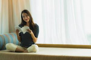 portret mooie jonge aziatische vrouw die een boek leest op de bank in de woonkamer foto