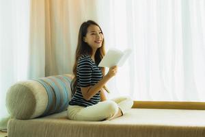 portret mooie jonge aziatische vrouw die een boek leest op de bank in de woonkamer foto