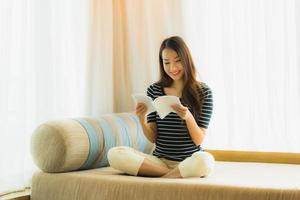 portret mooie jonge aziatische vrouw die een boek leest op de bank in de woonkamer foto