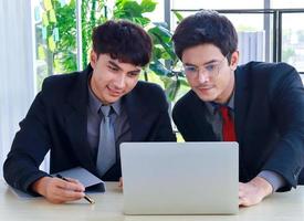 twee jonge zakenlieden zitten en werken op laptops in een modern kantoor, het zijn jonge, actieve zakenlieden foto