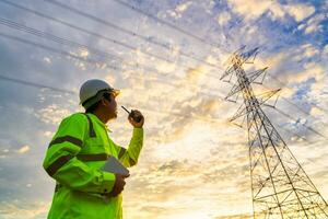 Aziatisch ingenieur gebruik radio cheques Bij een macht station voor planning werk door genereren elektriciteit van een hoog voltage transmissie toren Bij zonsondergang. foto