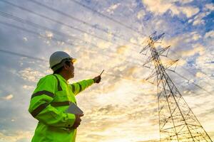 Aziatisch ingenieur cheques Bij een macht station voor planning werk door genereren elektriciteit van een hoog voltage transmissie toren Bij zonsondergang. foto