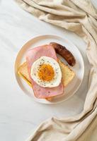 zelfgebakken brood geroosterde kaas, belegde ham en gebakken ei met varkensworst als ontbijt foto