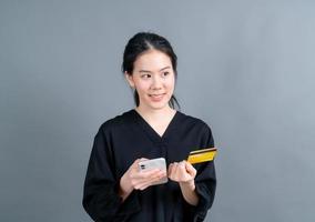 jong Aziatisch meisje dat een plastic creditcard toont terwijl ze een mobiele telefoon vasthoudt foto