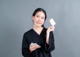 jong Aziatisch meisje dat een plastic creditcard toont terwijl ze een mobiele telefoon vasthoudt foto