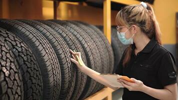 arbeider jong Azië vrouw vervelend gezicht medisch masker is controle kwaliteit van auto banden en controle de voorraad van auto banden in auto reparatie winkel op te slaan gedurende covid 19 epidemie. foto